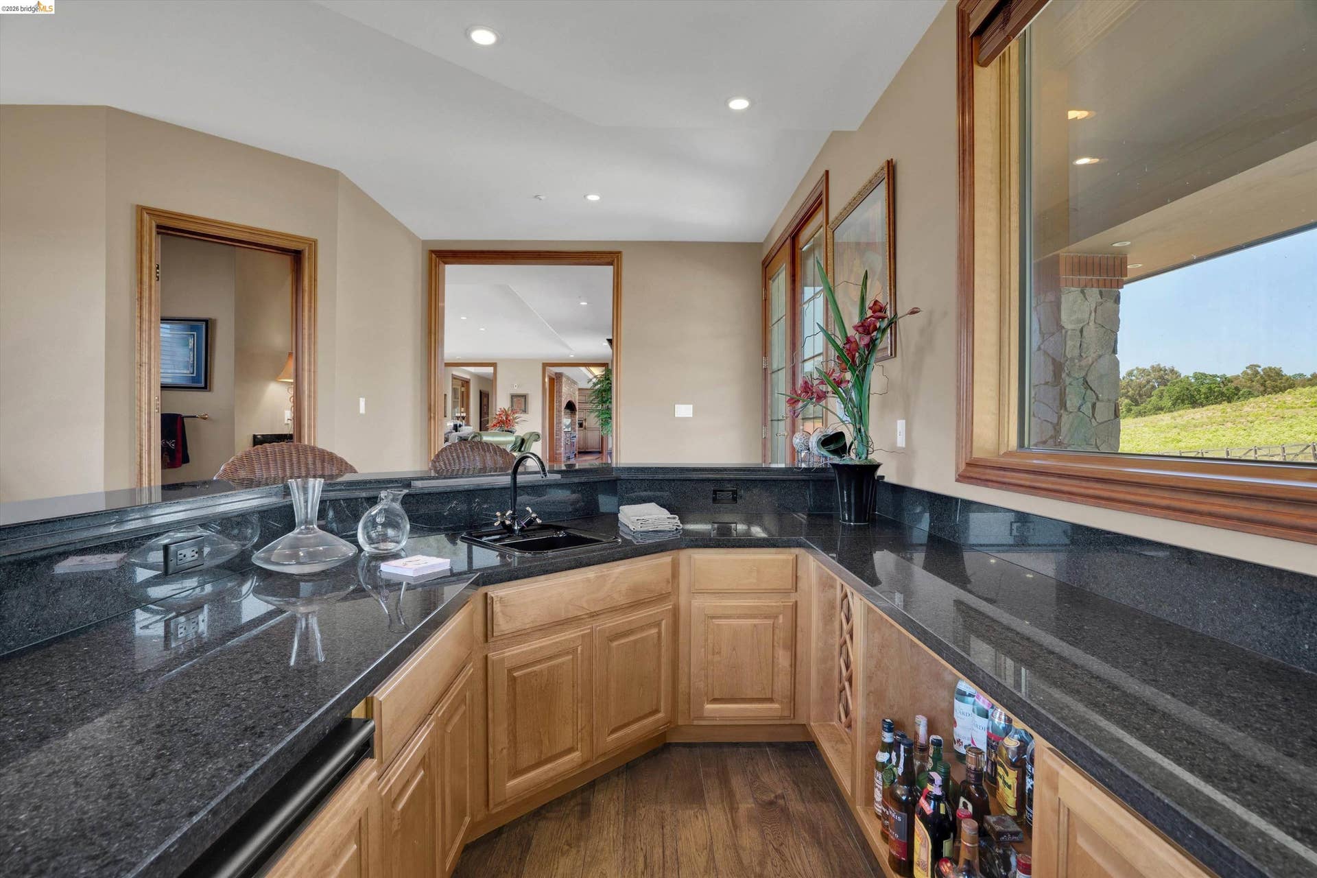 Wet bar featuring dark granite countertops, an undermount sink, recessed lighting, wood-finish flooring, and natural wood cabinetry