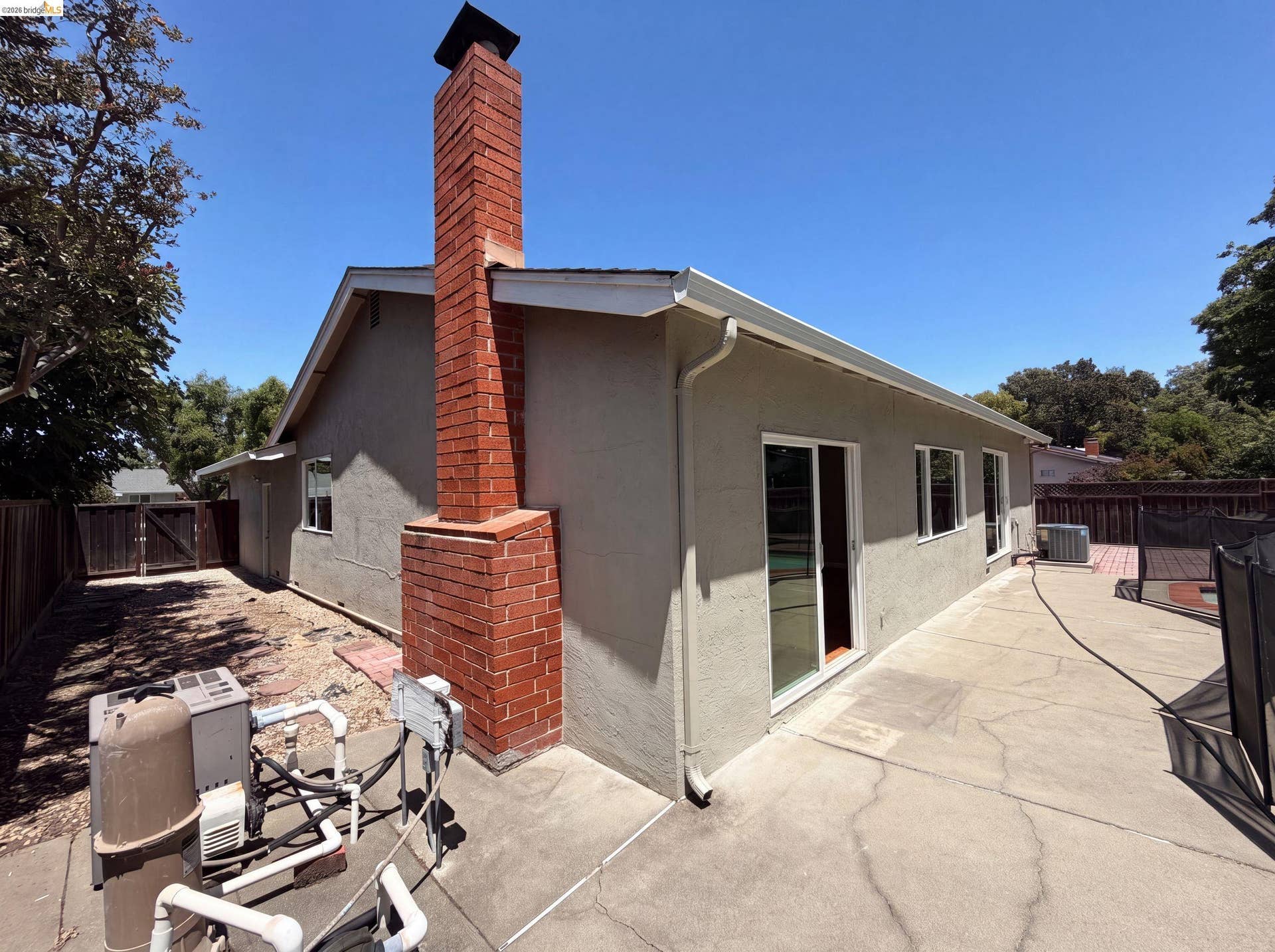 Exterior featuring a prominent brick chimney, stucco siding, and a concrete patio