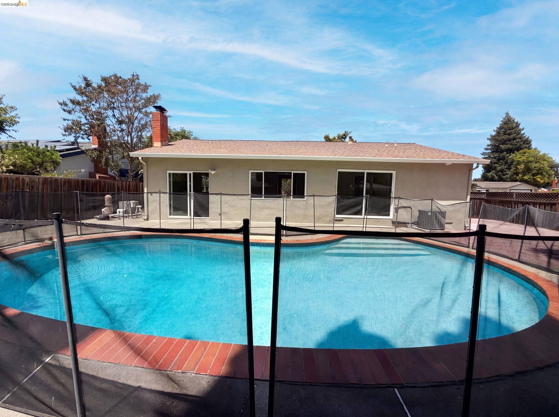 Backyard swimming pool featuring a safety fence, brick coping, and a surrounding patio