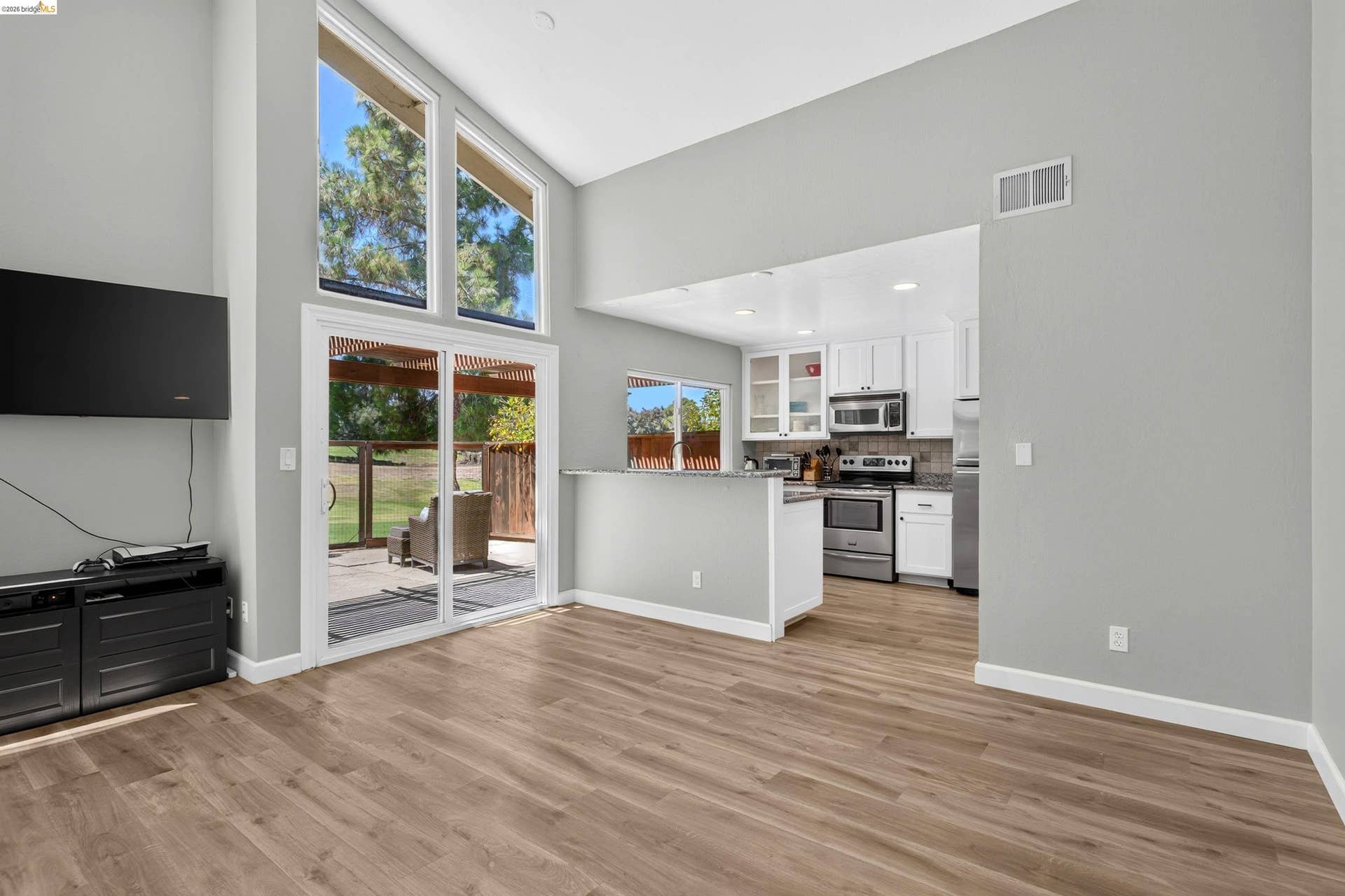 Spacious living area featuring wood-finish flooring, vaulted ceilings, and extensive natural light from large windows and a glass sliding door