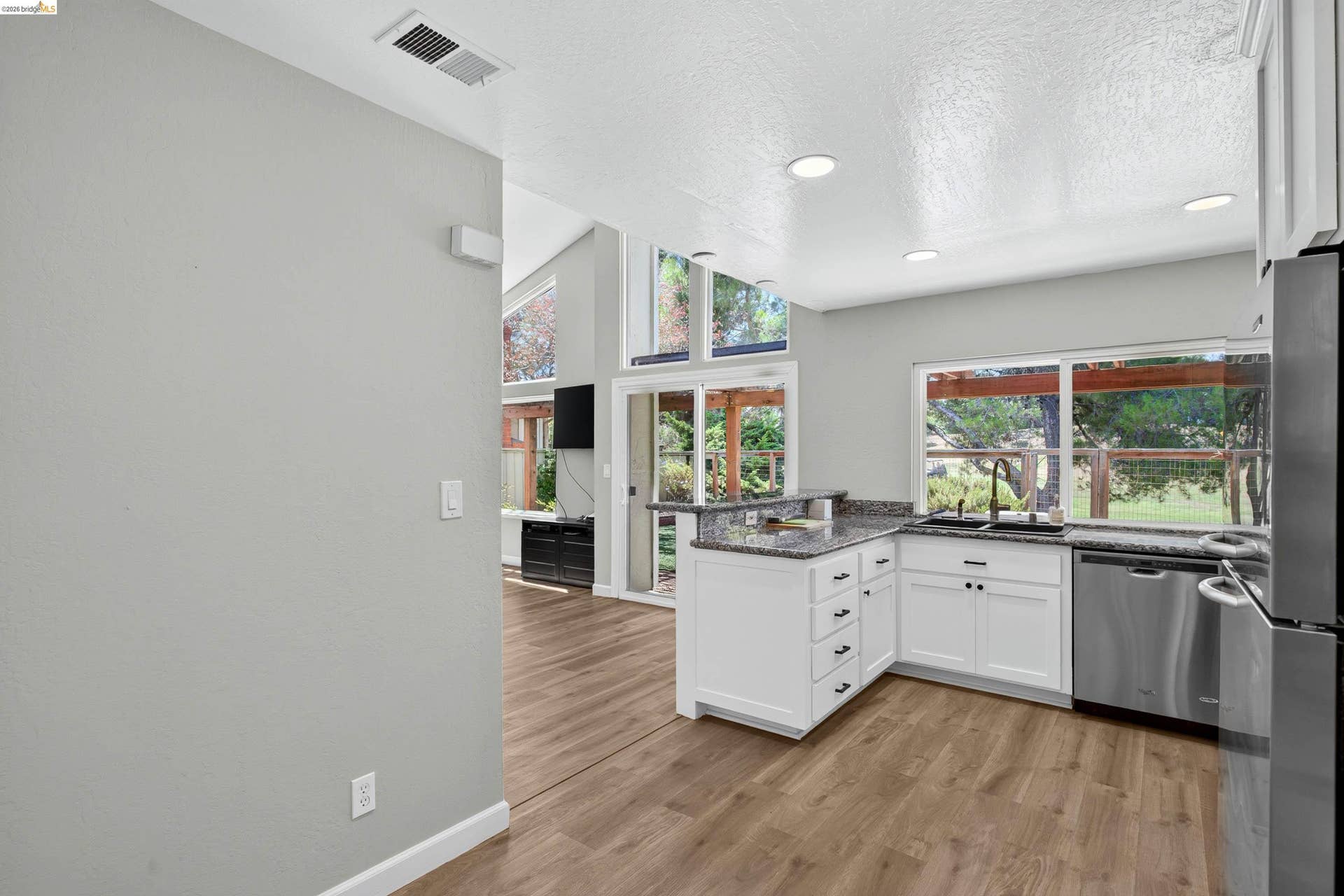 Kitchen with white shaker cabinetry, dark granite countertops, stainless steel appliances, and wood-finish flooring