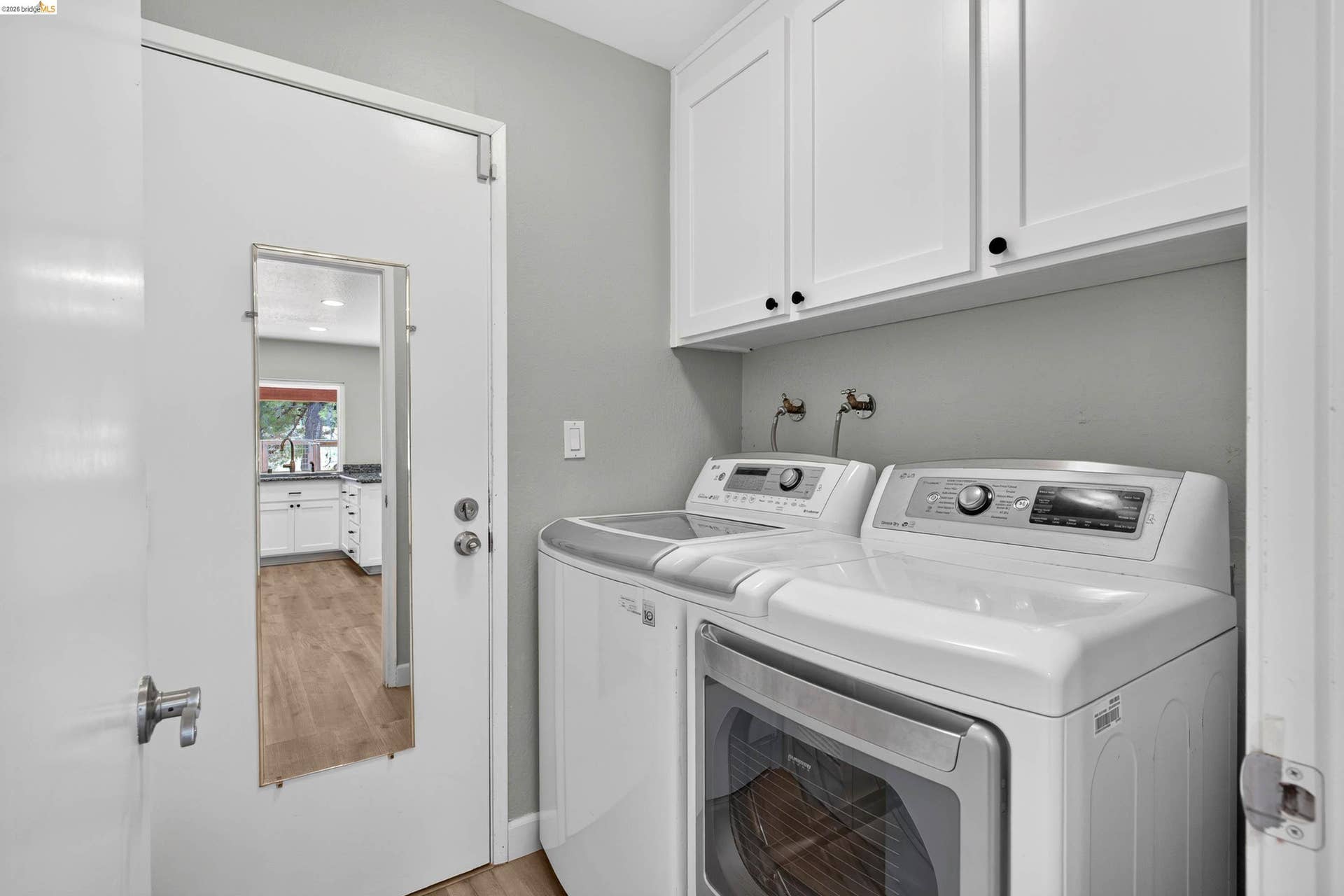 Dedicated laundry area featuring overhead white cabinetry with dark hardware