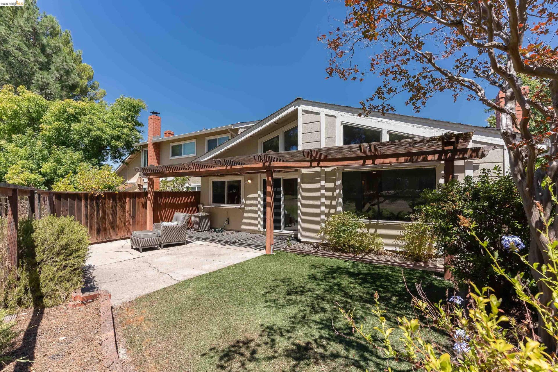 Property exterior featuring a pergola-covered patio, level lawn, mature landscaping, and a wood privacy fence