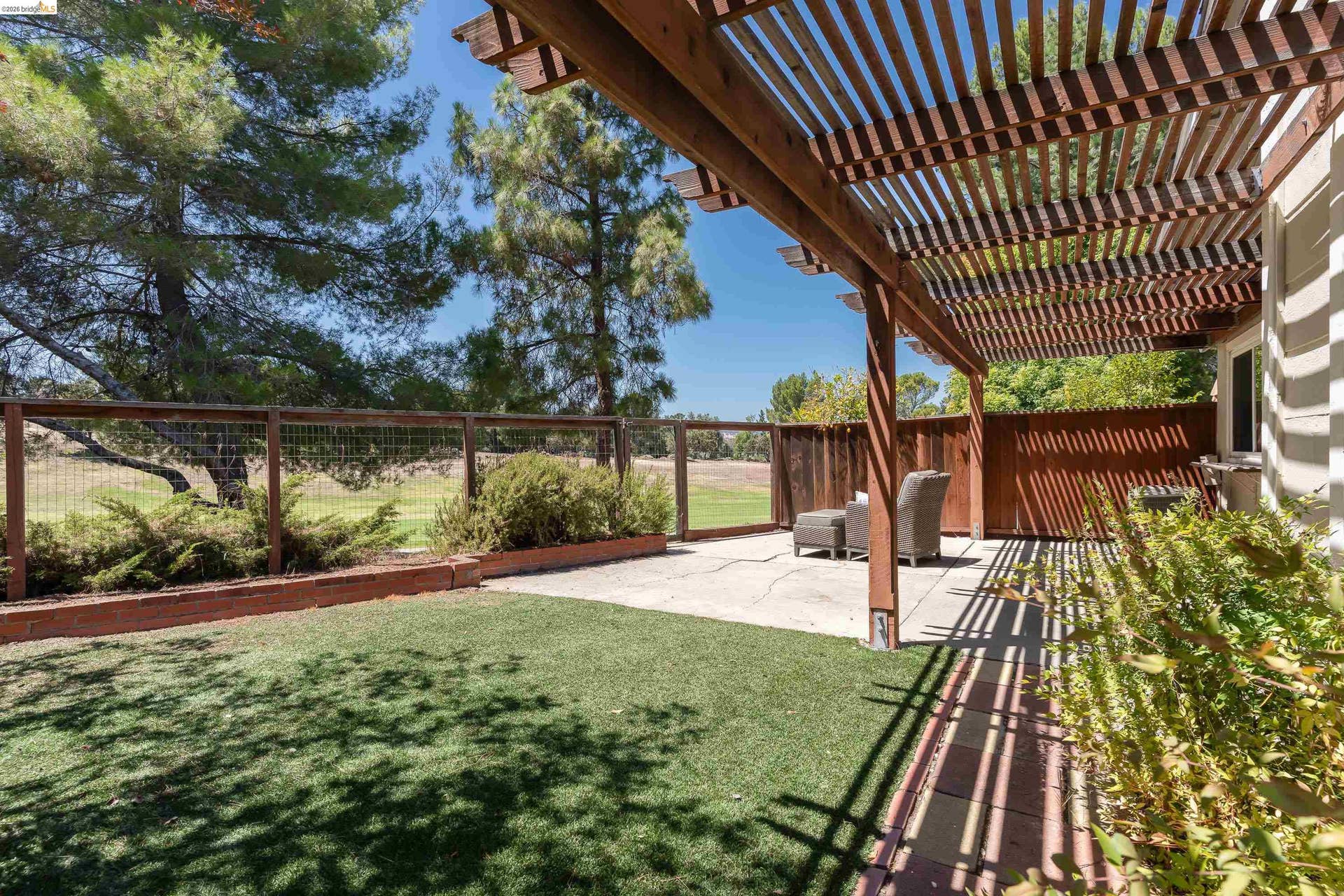 Outdoor patio with a slatted wood pergola, concrete surface, and adjacent artificial turf area