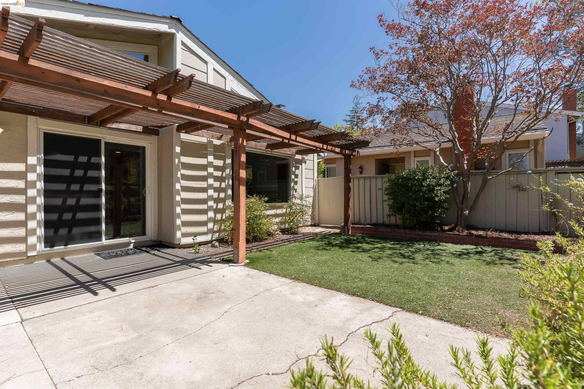 Rear patio area featuring a concrete surface, a wood pergola structure, and a sliding glass door