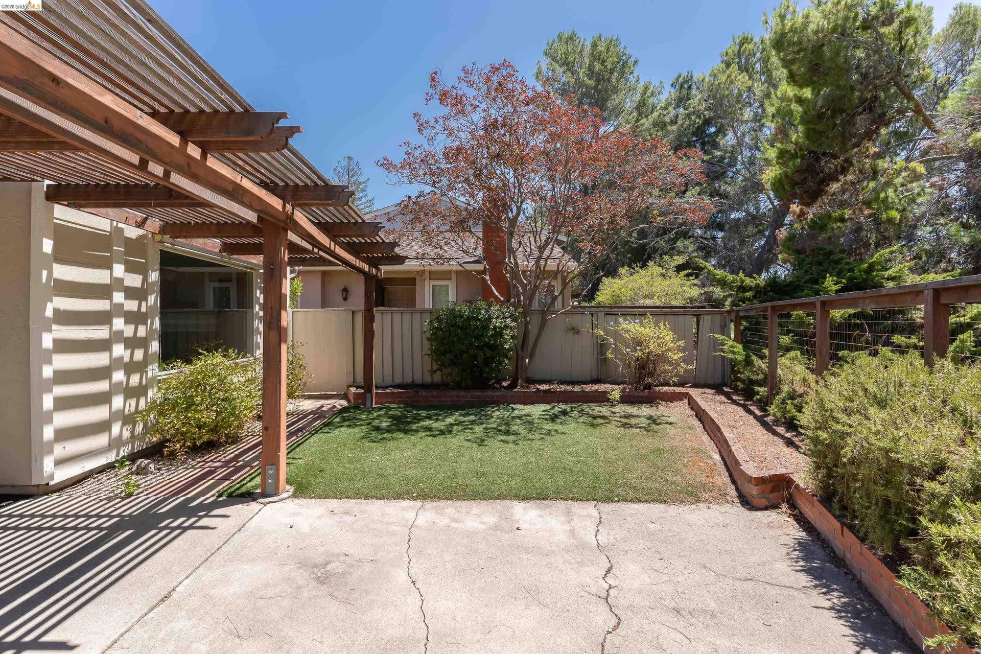 Outdoor patio area featuring a slatted wood pergola, concrete patio, and a section of artificial turf