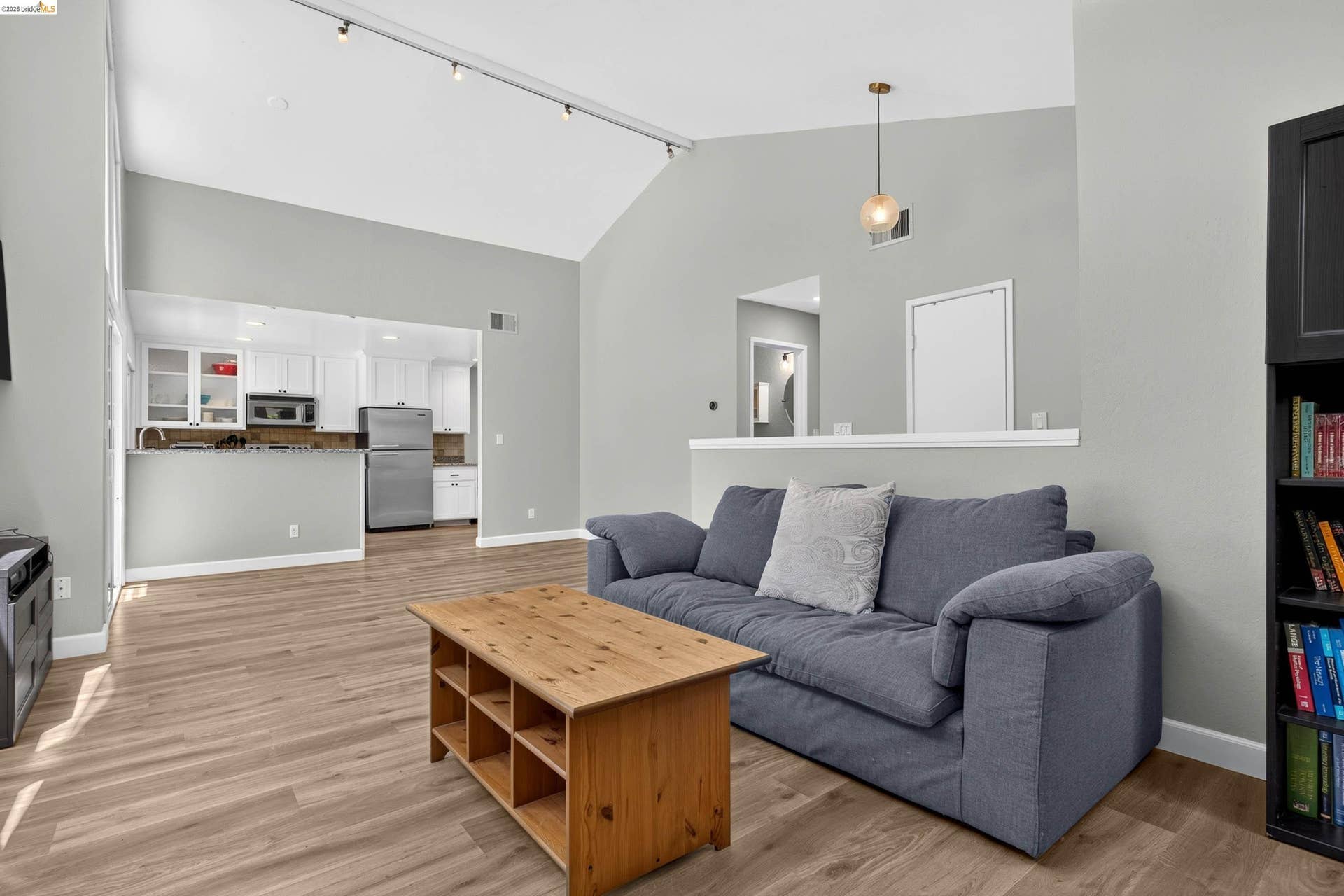 Open-concept living area with vaulted ceilings, track lighting, and wood-finish flooring