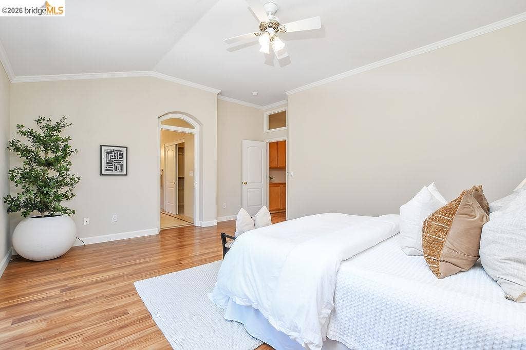 Vaulted ceiling with crown molding, wood-finish flooring, ceiling fan, and arched doorway