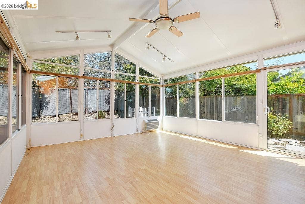 Vaulted ceiling sunroom with expansive windows, light wood-finish flooring, and a ceiling fan