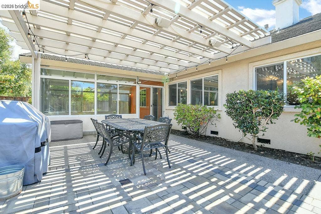 Expansive paved patio with an overhead pergola, string lighting, and direct exterior access