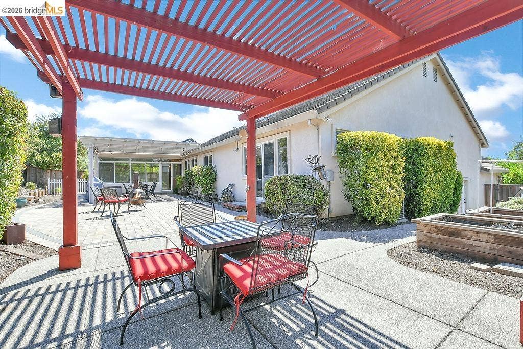 Red-stained pergola covering a concrete patio, extending to a paved patio area with an additional white pergola