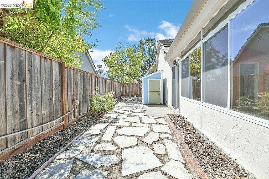 Flagstone pathway with a wooden privacy fence, stucco exterior, and multi-pane windows