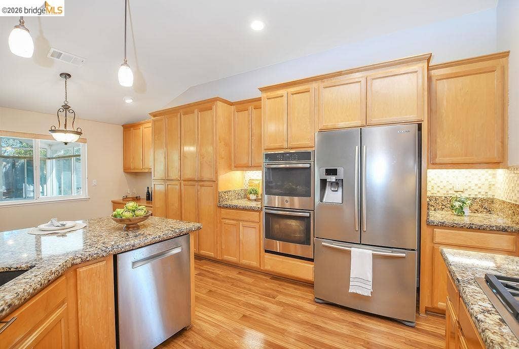 Kitchen featuring wood-finish flooring, light-toned cabinetry, granite countertops, and stainless steel appliances including a double oven and refrigerator