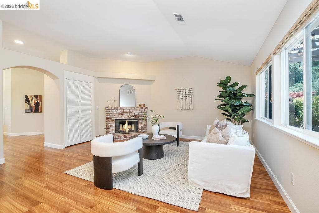 Living area featuring wood-finish flooring, a brick fireplace, arched doorway, and abundant natural light from multiple windows