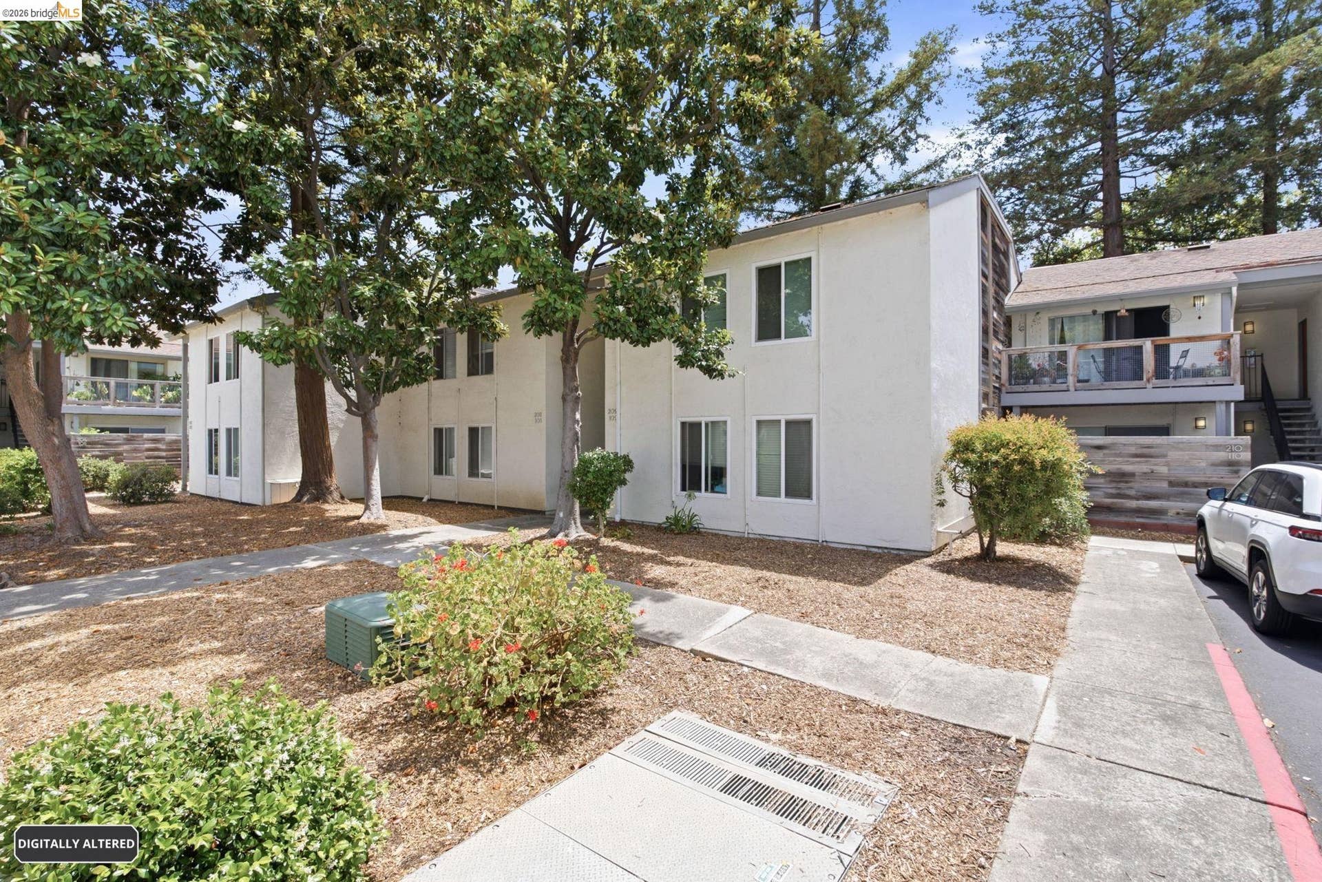 Multi-level residential building featuring a white exterior and mature trees