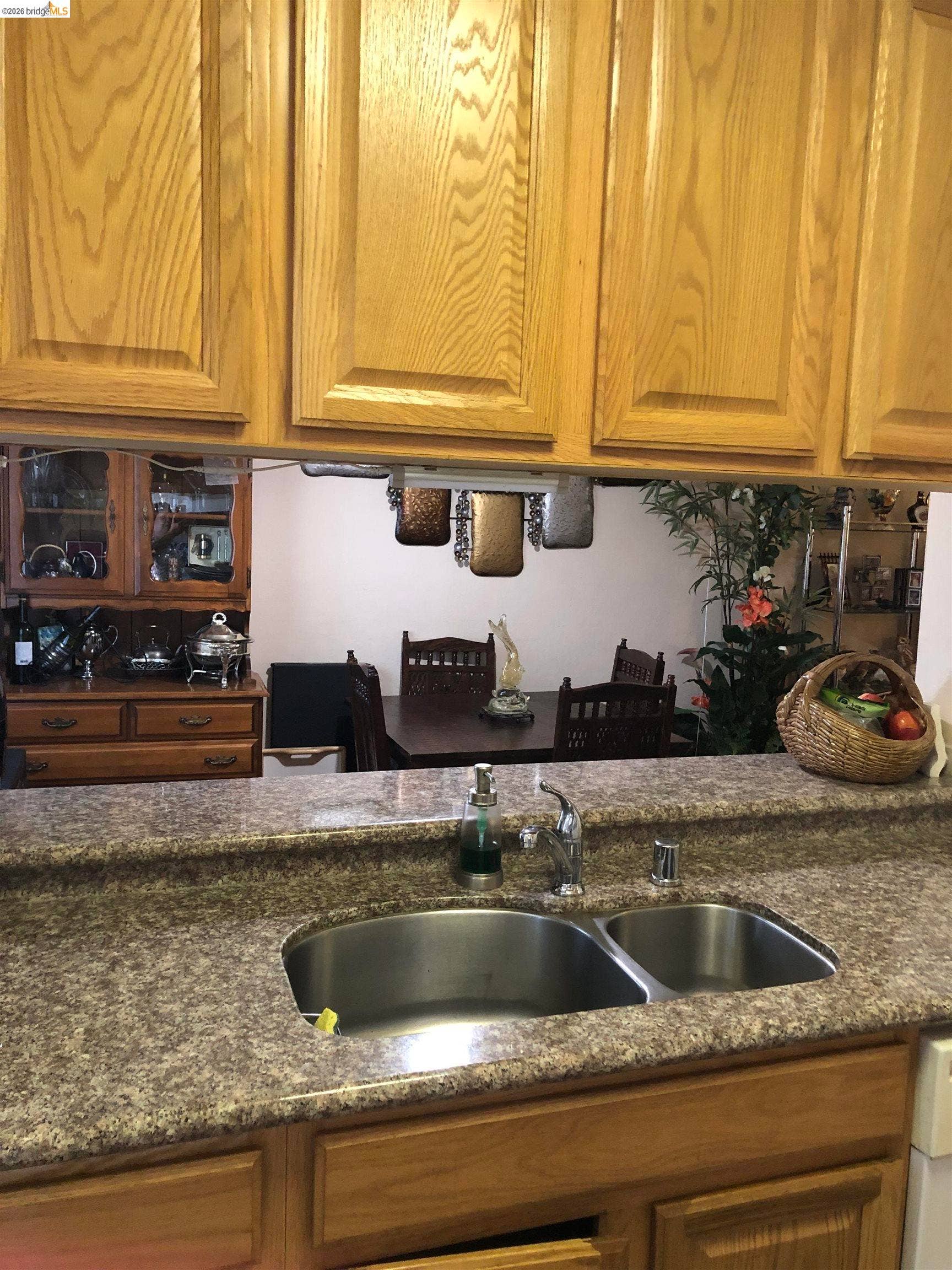 Light wood-finish cabinetry, speckled countertop, and a double basin stainless steel sink with a chrome faucet