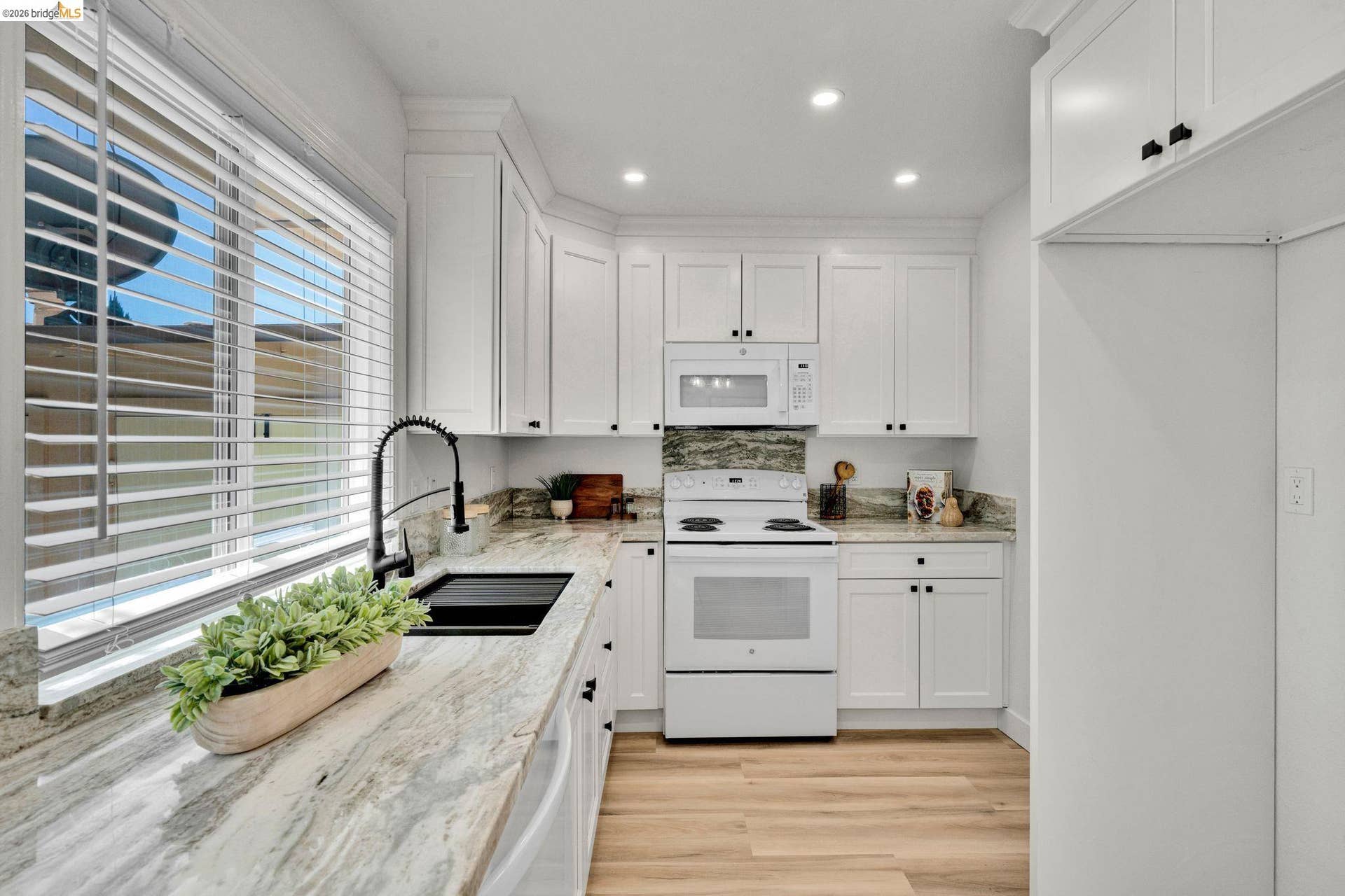 Modern kitchen featuring white cabinetry, light-toned wood-finish flooring, recessed lighting, and a window with blinds