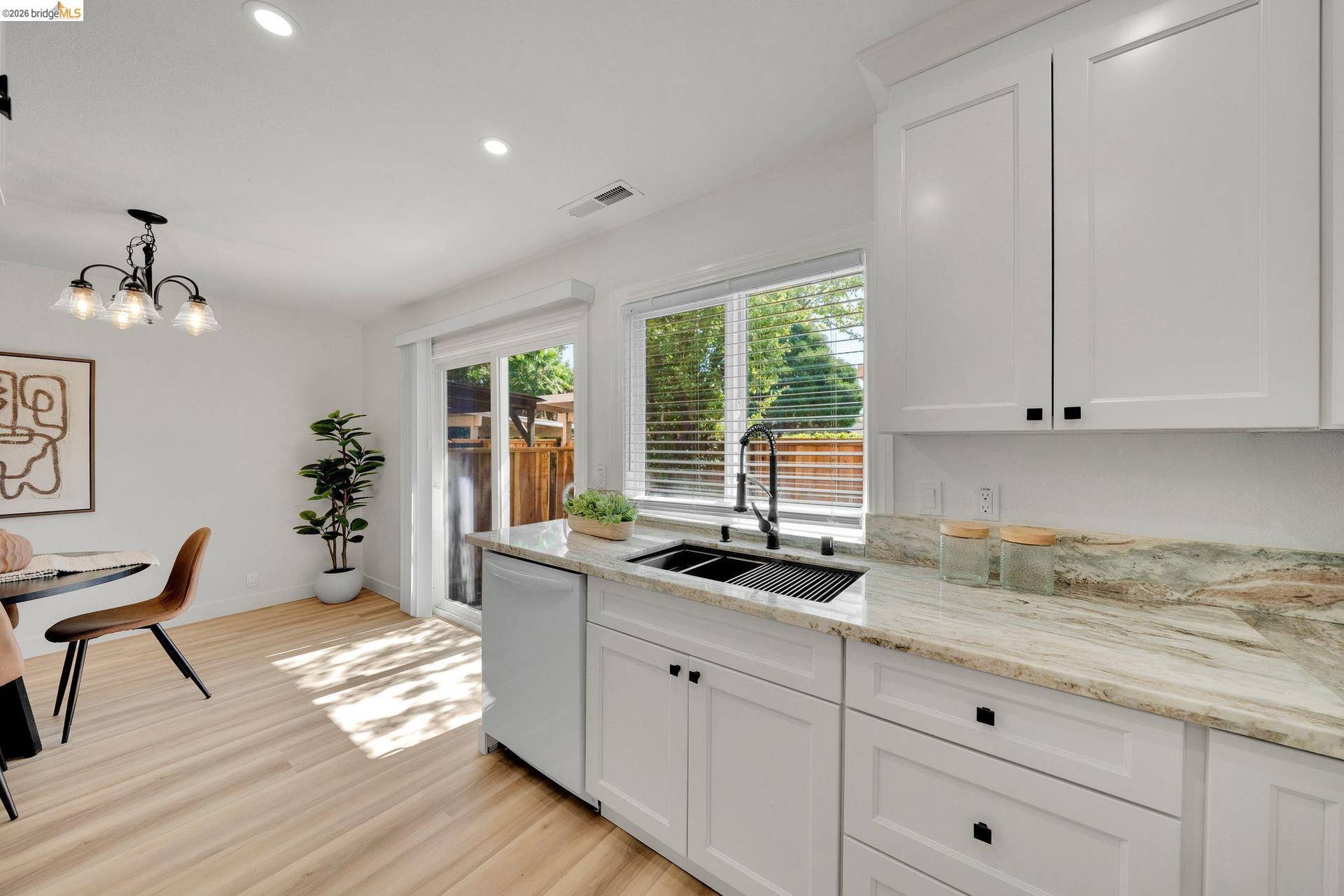 Modern kitchen featuring white shaker cabinetry, light-toned wood-finish flooring, a stainless steel dishwasher, and a black double basin sink with a matte black faucet