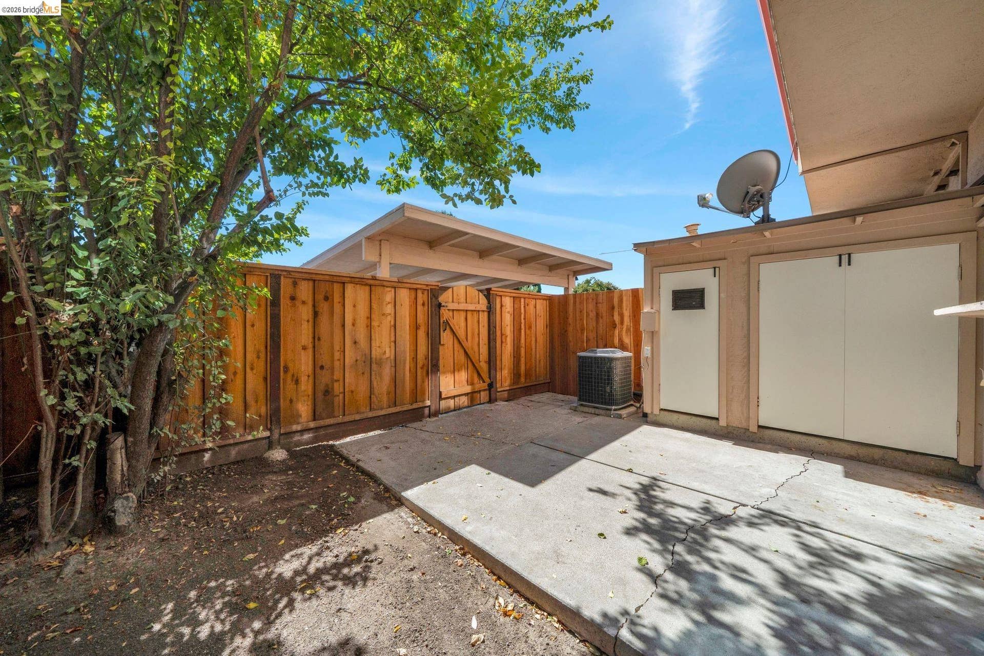 Private yard space featuring a wood fence, concrete patio, and mature trees