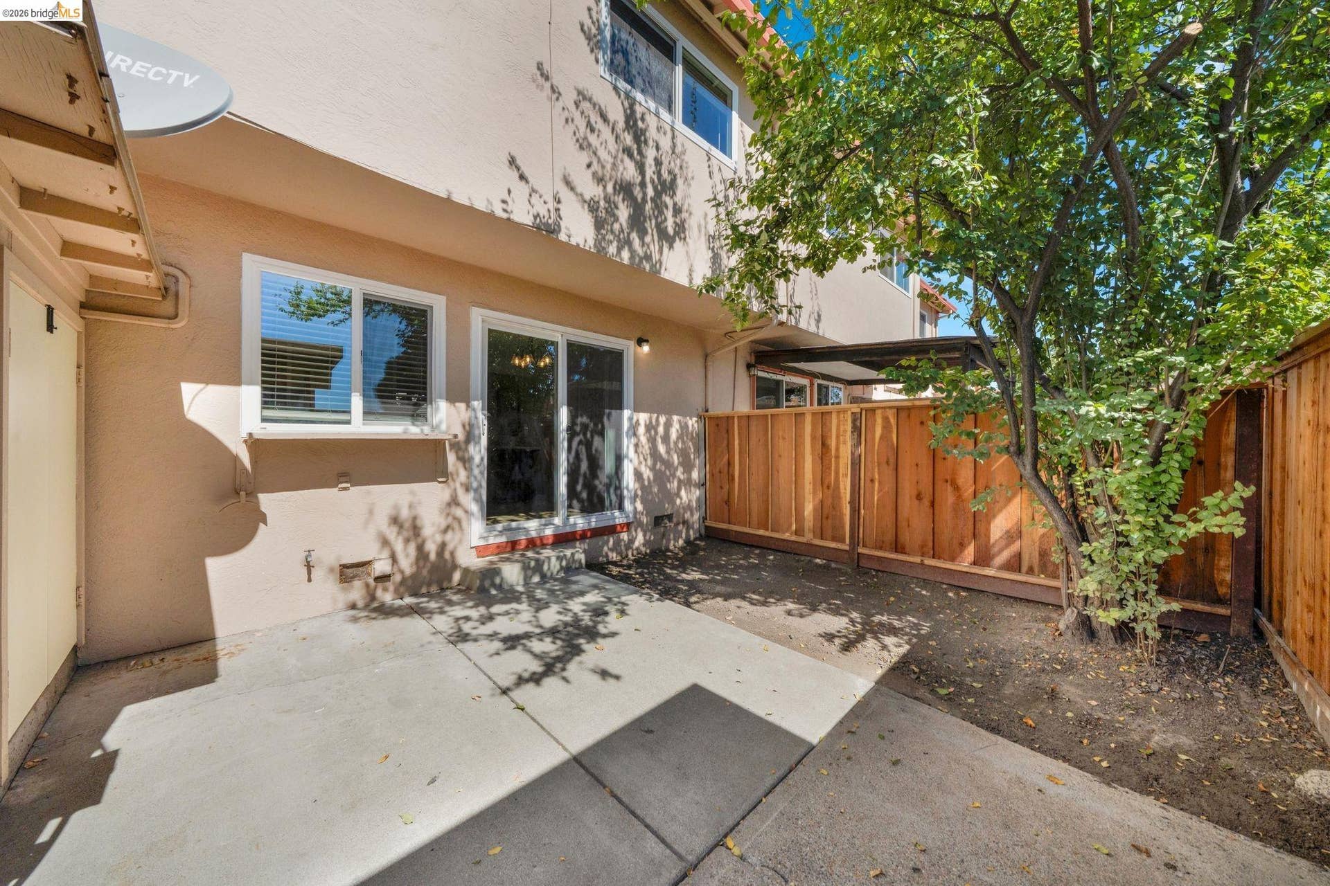 Private outdoor patio with a mature tree, wood fencing, and sliding glass door access
