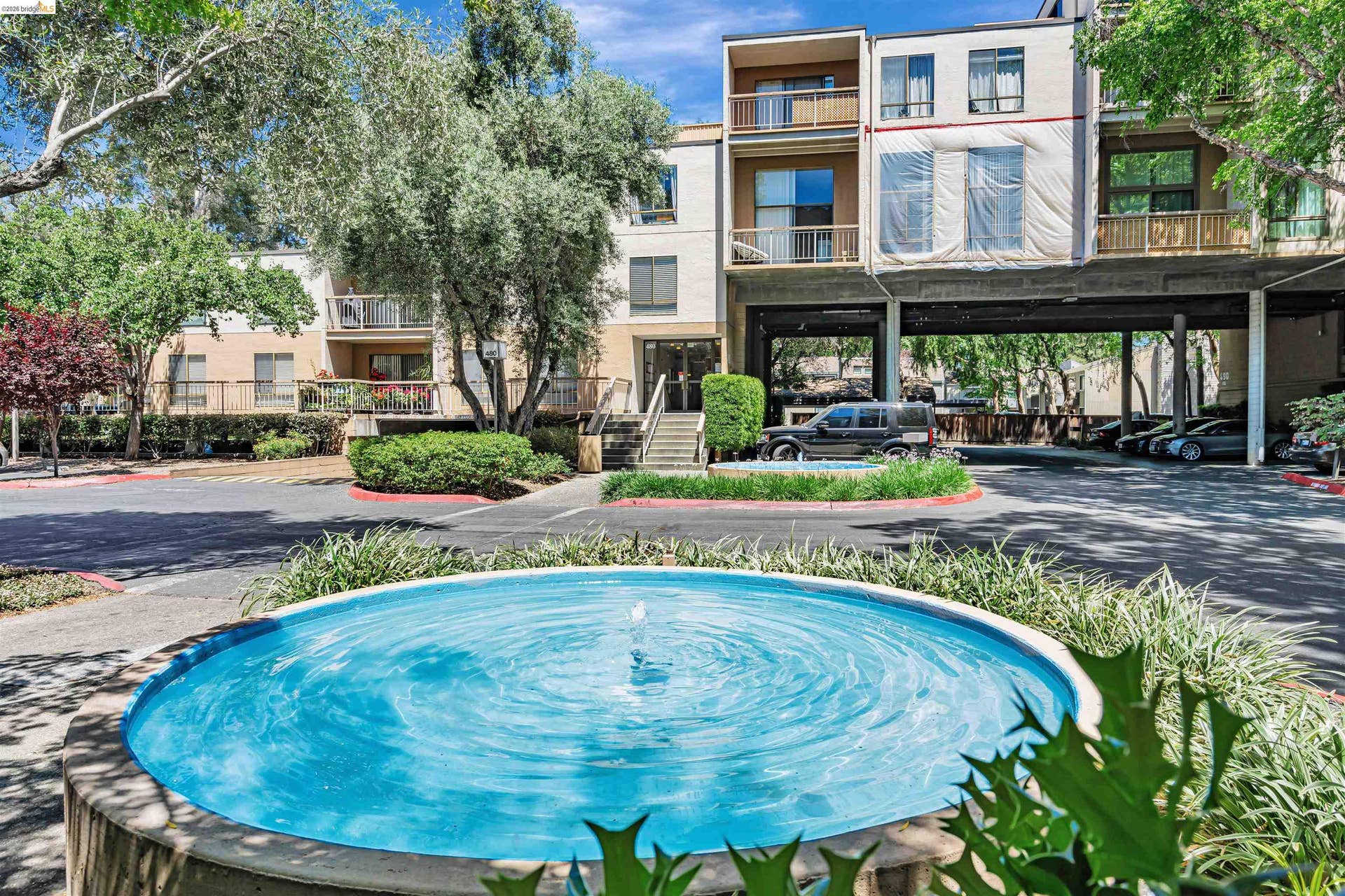 Central courtyard fountain, lush landscaping, covered parking structure, multi-story building architecture, balconies