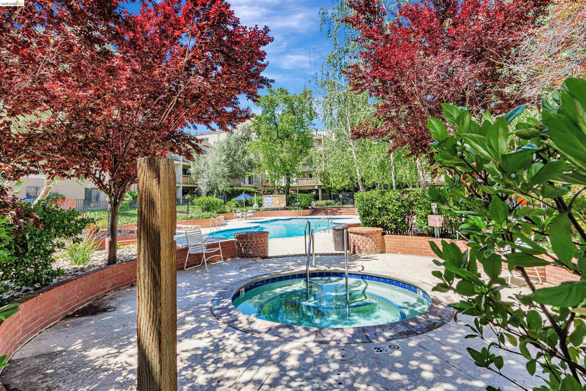 Circular hot tub with integrated steps, surrounded by a concrete patio and low brick retaining walls