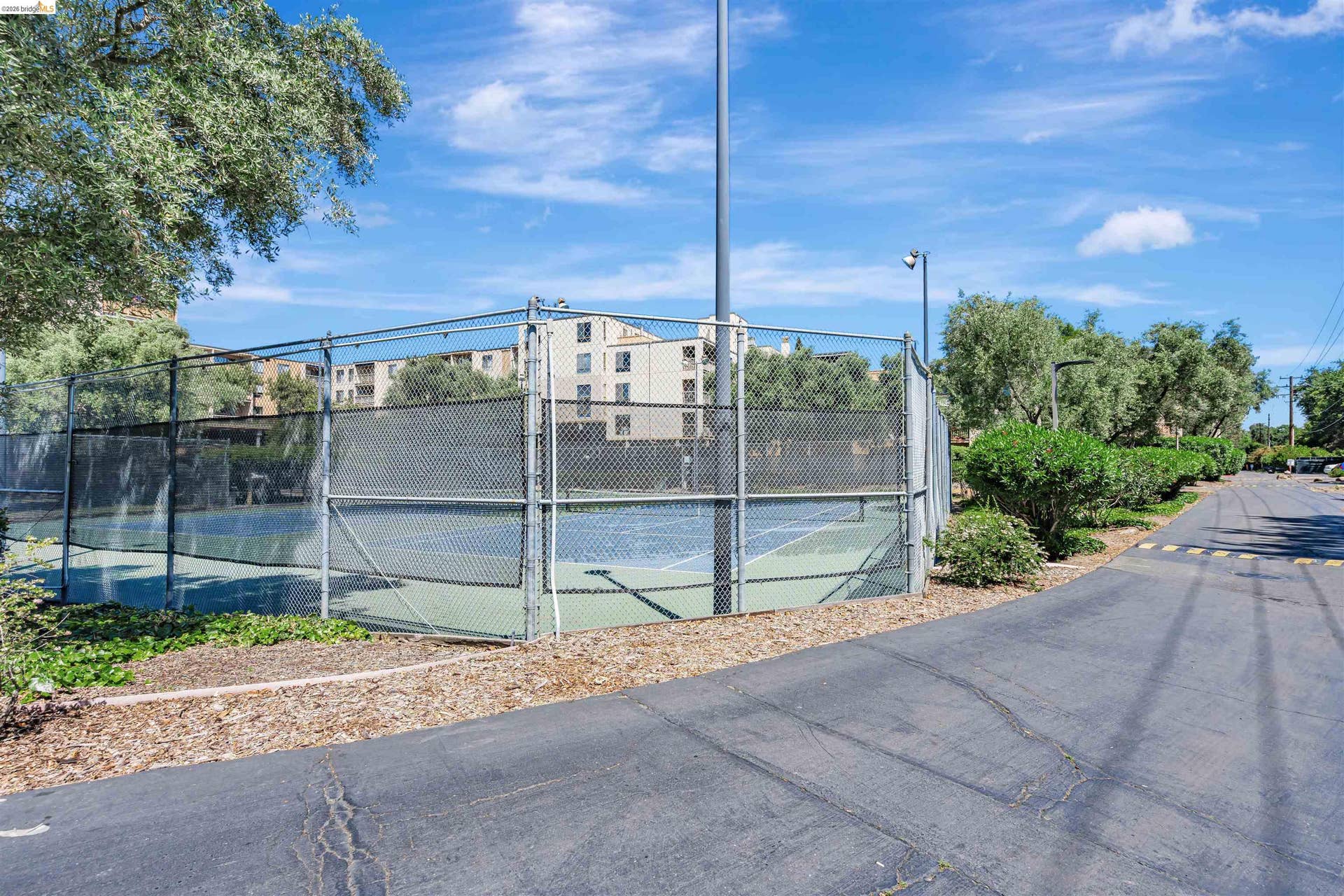 Hard surface tennis court enclosed by chain-link fencing