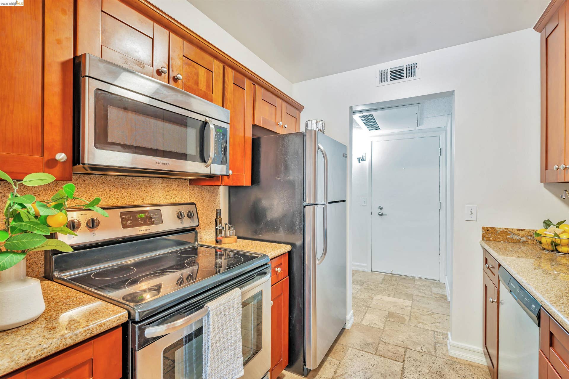 Wood-finish cabinetry, stainless steel appliances, stone-finish countertops, and tile flooring