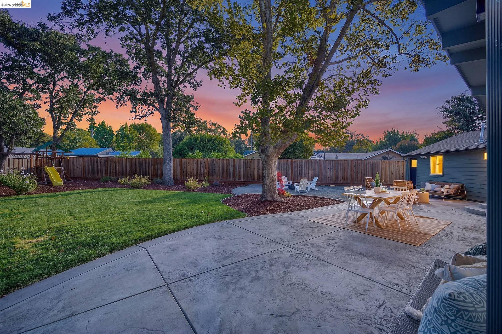 Expansive backyard featuring a large stamped concrete patio, manicured lawn, mature trees, and privacy fencing