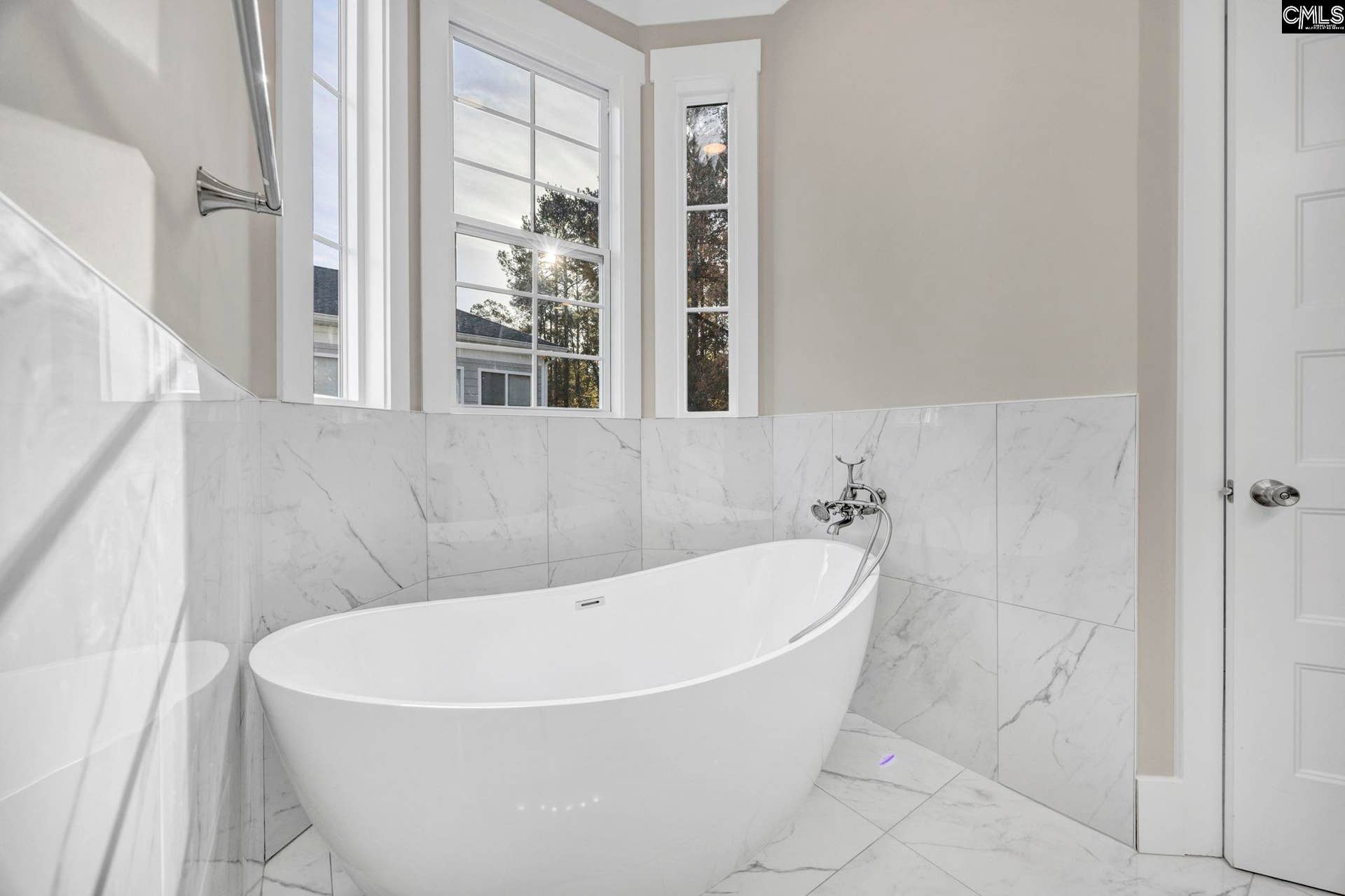 Elegant freestanding tub surrounded by beautiful tile and windows offering abundant natural light.